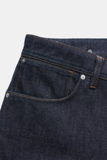 Nahaufnahme der Stone Island Jeans 'Indigo Denim - Raw' navy im Five-Pocket-Stil mit Loose Fit, Button Fly und Kompass-Badge am Bund, fotografiert von vorne schräg oben.