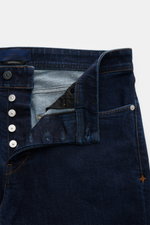 Close-up front view of Stone Island Jeans 'Stretch Indigo Denim - Rinsed' dark blue slim fit jeans with elastic cotton denim, tapered legs, and compass badge on waistband. Urban classic in a modern silhouette from STONE ISLAND's 'Denim' capsule collection