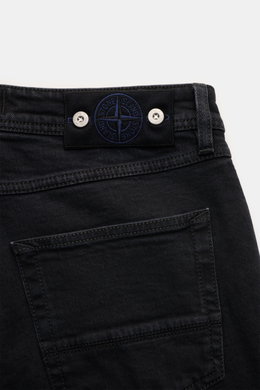Close-up rear view of Stone Island Jeans 'Stretch Black Denim - Rinsed' black, showing cotton denim fabric, slim fit, button fly, five-pocket style, and compass badge on waistband. Urban classic in a modern silhouette, stretch quality, very tapered.