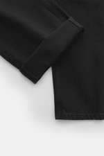 Close-up of The Row Jeans 'Vanya' black showing black-textured denim fabric with subtle tonal variations and folded hem, photographed from above.