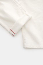Nahaufnahme der Ace Denim Jeans 'AD 53' offwhite aus Selvedge-Denim mit leichtem Stretch, weichem Griff, Tapered Fit, Button Fly, Five-Pocket-Stil und besticktem Patch, fotografiert von schräg oben.