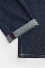 Nahaufnahme der Barmas Venezia Jeans 'Denver' navy, schmal zulaufend, Regular Fit, Five-Pocket-Stil, Button Fly, Denim aus Baumwolle mit Cashmere, weich, leicht elastisch, Detailansicht Saum mit geprägtem Leather Patch.