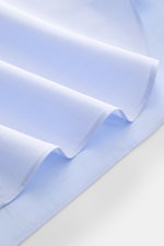 Close-up of folded light blue fabric showcasing the smooth twill cotton of the Borrelli Business Shirt 'Luciano' Shark Collar, photographed from a top-side angle. Masterful craftsmanship down to the smallest detail: The 'Luciano' shirt by BORRELLI embodie