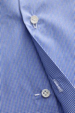 Close-up front detail of Borrelli Business shirt 'Nando' shark collar dark blue/white checked, showing fine cotton poplin, slim fit, French button placket with mother-of-pearl buttons, photographed from a top angle. Masterful craftsmanship down to the sma
