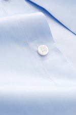 Nahaufnahme des Fray Hemd Haifisch-Kragen 'Nello' hellblau aus reiner Baumwolle mit Slim Fit, Haifischkragen, klassischer Sportmanschette, leicht griffiger Haptik und leicht gerundetem Saumverlauf, fotografiert aus schräger Perspektive.