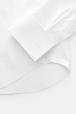 Nahaufnahme des gerundeten Saumverlaufs und der eleganten Umschlagmanschette des BRAUN Hamburg Smokinghemds Kläppchen-Kragen weiß, Popeline aus reiner Baumwolle, glatter Griff, Extra Slim Fit, verdeckte Knopfleiste mit Perlmuttknöpfen.