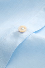 Close-up from above of a beige button on the light blue von Braun Linen shirt shark collar light blue, showing pure linen texture.

Description: <p><span class="_fadeIn_m1hgl_8">Effortlessly </span><span class="_fadeIn_m1hgl_8">lightweight</span><span cla