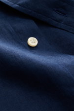 Dunkelblauer Stoff mit feiner Leinenstruktur und Knopf, Detailaufnahme aus nächster Nähe eines Polo Ralph Lauren Leinenhemd Button-Down-Kragen türkis.