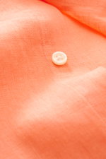 Nahaufnahme eines weißen Knopfes und der typischen Materialstruktur des Polo Ralph Lauren Leinenhemd Button-Down-Kragen orange aus reiner, leichter, luftiger Leinenqualität, fotografiert aus schräger Perspektive.