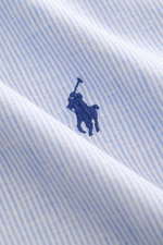 Nahaufnahme aus schräger Perspektive des sommerlichen Polo Ralph Lauren Oxford-Hemd Haifisch-Kragen hellblau/weiß gestreift mit weichem Griff, elastischer Qualität und Polospieler-Stitching.