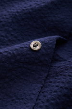 Close-up view of the navy seersucker fabric and button detail on the 04651/ A trip in a bag Seersucker shirt Kent collar navy, showcasing its textured cotton material.

<p><span class="_fadeIn_m1hgl_8">Effortlessly </span><span class="_fadeIn_m1hgl_8">cas