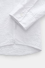 Close-up side view of the white 04651/ A trip in a bag Seersucker shirt Kent collar white showing seersucker texture, cuff, hem vents, and side label.

Description: <p><span class="_fadeIn_m1hgl_8">Effortlessly </span><span class="_fadeIn_m1hgl_8">casual<