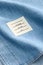 Nahaufnahme des Thom Browne Jeanshemd Button-Down-Kragen rauchblau mit Label, reine Baumwolle, leicht griffige Haptik, Regular Fit.