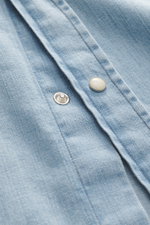 Close-up front angled view of Ace Denim Denim shirt smoky blue highlighting applied snap button placket, pure cotton fabric, soft touch, slim fit, narrow collar, applied chest pockets, western-style yoke, classic sport cuff, and rounded hem.