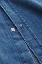 Nahaufnahme des Ace Denim Jeanshemd blau, Fokus auf die aufgesetzte Druckknopfleiste aus reiner Baumwolle mit weichem Griff, fotografiert aus schräger Perspektive.