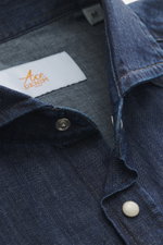 Nahaufnahme aus schräger Perspektive des Ace Denim Jeanshemd dunkelblau mit schmalem Kragen, aufgesetzter Druckknopfleiste, reiner Baumwolle, weichem Griff, Slim Fit, aufgesetzten Brusttaschen, Schulterpasse im Western-Stil, klassischer Sportmanschette un