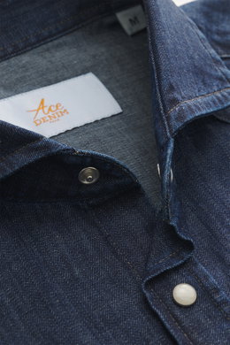 Nahaufnahme aus schräger Perspektive des Ace Denim Jeanshemd dunkelblau mit schmalem Kragen, aufgesetzter Druckknopfleiste, reiner Baumwolle, weichem Griff, Slim Fit, aufgesetzten Brusttaschen, Schulterpasse im Western-Stil, klassischer Sportmanschette un