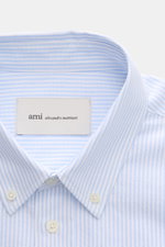 Ami Paris Casual Shirt Button-Down Collar Light Blue/White Striped shown from top front close-up, modern classic with pure cotton, soft touch, oversized fit, classic stripe design, patch button placket, sport cuff, slightly rounded hemline. Modern interpr