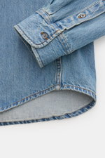 Nahaufnahme eines rauchblauen Ami Paris Jeanshemd Button-Down-Kragen, fotografiert von oben auf Manschette und Saum aus reiner Baumwolle mit leichter Struktur.
