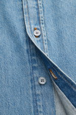 Nahaufnahme des Ami Paris Jeanshemds Button-Down-Kragen rauchblau aus reiner Baumwolle, Detail der Knopfleiste und leichter Denim-Struktur.