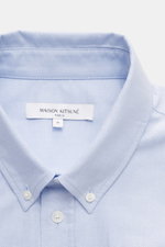 Close-up front view of Maison Kitsuné Oxford shirt button-down collar light blue showcasing button-down collar, pure cotton Oxford fabric, soft feel, regular fit, signature logo stitching, classic barrel cuffs, inverted pleat on back, and rounded hem.