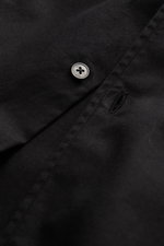 Schwarzer Knopf und Knopflasche in Nahaufnahme, Detail des 04651/ A trip in a bag Casual Hemd 'Winter Cotton' Kent-Kragen schwarz aus Baumwoll-Gabardine.