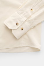 Close-up of the sleeve and hemline of the Brunello Cucinelli Cord Shirt Shark Collar Cream, photographed from above, showcasing the fine cotton corduroy fabric, slim fit, snap button placket, classic sport cuff, and straight hemline.