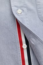 Close-up front view of Thom Browne Short sleeve shirt button-down collar smoky blue, made of pure cotton Oxford fabric with button placket featuring red, white, and navy stripes. A modern interpretation of a classic: This stylish short sleeve shirt by THO