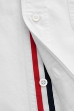 Close-up front view of Thom Browne Short-sleeve shirt button-down collar white showing button placket with red, white, and navy stripes, pure cotton Oxford fabric, soft feel, regular fit, patch breast pocket, back yoke with inverted pleat and hanging loop