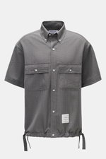 Vorderansicht des Thom Browne Seersucker-Kurzarmhemds Button-Down-Kragen dunkelgrau mit Oversized-Fit, zwei geknöpften Brusttaschen, regulierbarem Saum und strukturierter Woll-Seersucker-Qualität.