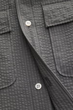 Nahaufnahme des Thom Browne Seersucker-Kurzarmhemd Button-Down-Kragen dunkelgrau mit strukturierter Wollqualität, Perlmuttknöpfen und geknöpften Brusttaschen.