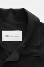 Nahaufnahme von Ami Paris Kurzarmhemd 'Boxy' Kubanischer Kragen schwarz, reine Viskose, weicher Griff, Oversized Fit, französische Knopfleiste, Logo-Stitching, gerundeter Saum, von oben fotografiert.