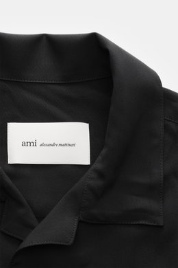 Nahaufnahme von Ami Paris Kurzarmhemd 'Boxy' Kubanischer Kragen schwarz, reine Viskose, weicher Griff, Oversized Fit, französische Knopfleiste, Logo-Stitching, gerundeter Saum, von oben fotografiert.