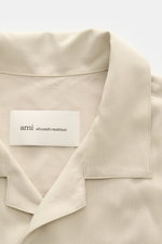 Nahaufnahme des Ami Paris Kurzarmhemds 'Boxy' Kubanischer Kragen sand, mit Oversized Fit, weicher Viskose, französischer Knopfleiste und Logo-Stitching, von oben fotografiert.