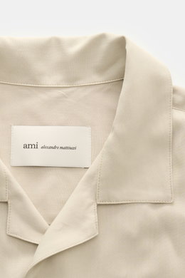 Nahaufnahme des Ami Paris Kurzarmhemds 'Boxy' Kubanischer Kragen sand, mit Oversized Fit, weicher Viskose, französischer Knopfleiste und Logo-Stitching, von oben fotografiert.