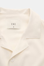 Ché Short sleeve shirt 'Valbonne' Cuban collar cream shown from above, featuring oversized fit, Cuban collar, French button placket, soft viscose fabric, and contrasting sleeve details. The short sleeve shirt 'Valbonne' by CHÉ encapsulates summery nonchal