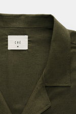 Nahaufnahme des offenen Kragens und des Labels des Ché Kurzarmhemd 'Inigo' Offener Kragen dark olive aus Leinen-Baumwoll-Mix, Oversized Fit, Häkel-Detail, fotografiert von oben.