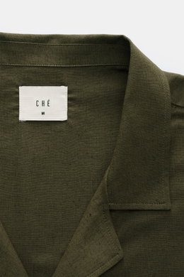 Nahaufnahme des offenen Kragens und des Labels des Ché Kurzarmhemd 'Inigo' Offener Kragen dark olive aus Leinen-Baumwoll-Mix, Oversized Fit, Häkel-Detail, fotografiert von oben.