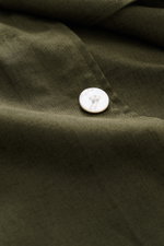 Nahaufnahme des Ché Kurzarmhemds 'Inigo' Offener Kragen dark olive aus Leinen-Baumwoll-Mix mit weißem Knopf, sichtbar Häkel-Detail am Saum.