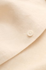 Close-up front view of the Percival Linen short sleeve shirt Cuban collar beige focusing on the fabric texture and button. Cool, lightweight and antibacterial: Linen’s natural qualities make it the perfect summer material. PERCIVAL has chosen the sustaina