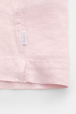 Nahaufnahme des Saumendes in roséfarbenem Leinen mit kleinem Weblabel 04651, Detail des 04651/ A trip in a bag Leinen-Kurzarmhemd Kubanischer Kragen rosé mit geradem Saum und kurzen Saumschlitzen, aus reiner Leinenqualität mit luftiger, materialtypischer 