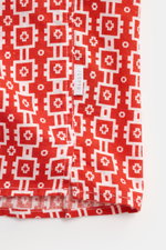 Close-up view of the hem and side seam of the 04651/ A trip in a bag Short-sleeved shirt 'Tiles' red/white patterned, showing a distinctive red and white geometric pattern with a small woven label on the side seam. <p>Experience the urge to travel with th