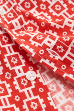 Close-up front view of the 04651/ A trip in a bag Short-sleeved shirt 'Tiles' red/white patterned, showing a distinctive red and white geometric tile pattern, white buttons, and stitched buttonhole details on a linen-cotton blend fabric. <p>Experience the