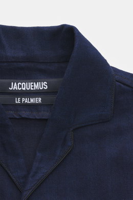 Nahaufnahme des offenen Kragens des Jacquemus Denim Kurzarmhemd dunkelblau aus reine Baumwolle, Regular Fit mit aufgesetzter Brusttasche und dekorativer J-Schlaufe, fotografiert aus schräger Frontperspektive.