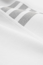 Nahaufnahme des weißen Thom Browne Poloshirts aus reiner Baumwolle mit strukturierter Oberfläche und markentypischem Streifen-Logo.