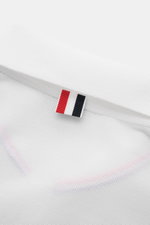 Nahaufnahme des weißen Thom Browne Poloshirts, Rückseite mit markentypischem roten, weißen und schwarzen Streifen-Logo am Kragen.