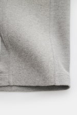 Nahaufnahme des Thom Browne Poloshirts grau meliert von der Saumkante, zeigt Slim Fit, reine Baumwolle, leicht griffige Struktur.
