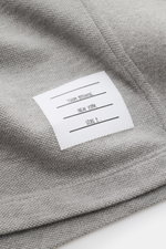 Nahaufnahme des Thom Browne Poloshirts grau meliert aus reiner Baumwolle, zeigt das gewebte Material und das weiße Markenlabel.