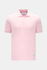 Thom Browne Poloshirt rosé, frontal fotografiert, Slim Fit aus reiner Baumwolle mit klassischem Polokragen, Fünf-Knopf-Leiste, Rippbündchen, elastischen Seiteneinsätzen und markentypischem Streifen-Logo.