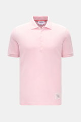Thom Browne Poloshirt rosé, frontal fotografiert, Slim Fit aus reiner Baumwolle mit klassischem Polokragen, Fünf-Knopf-Leiste, Rippbündchen, elastischen Seiteneinsätzen und markentypischem Streifen-Logo.